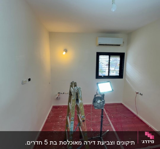 סולם, דלי צבע, מנורה וחדר צבוע בלבן
